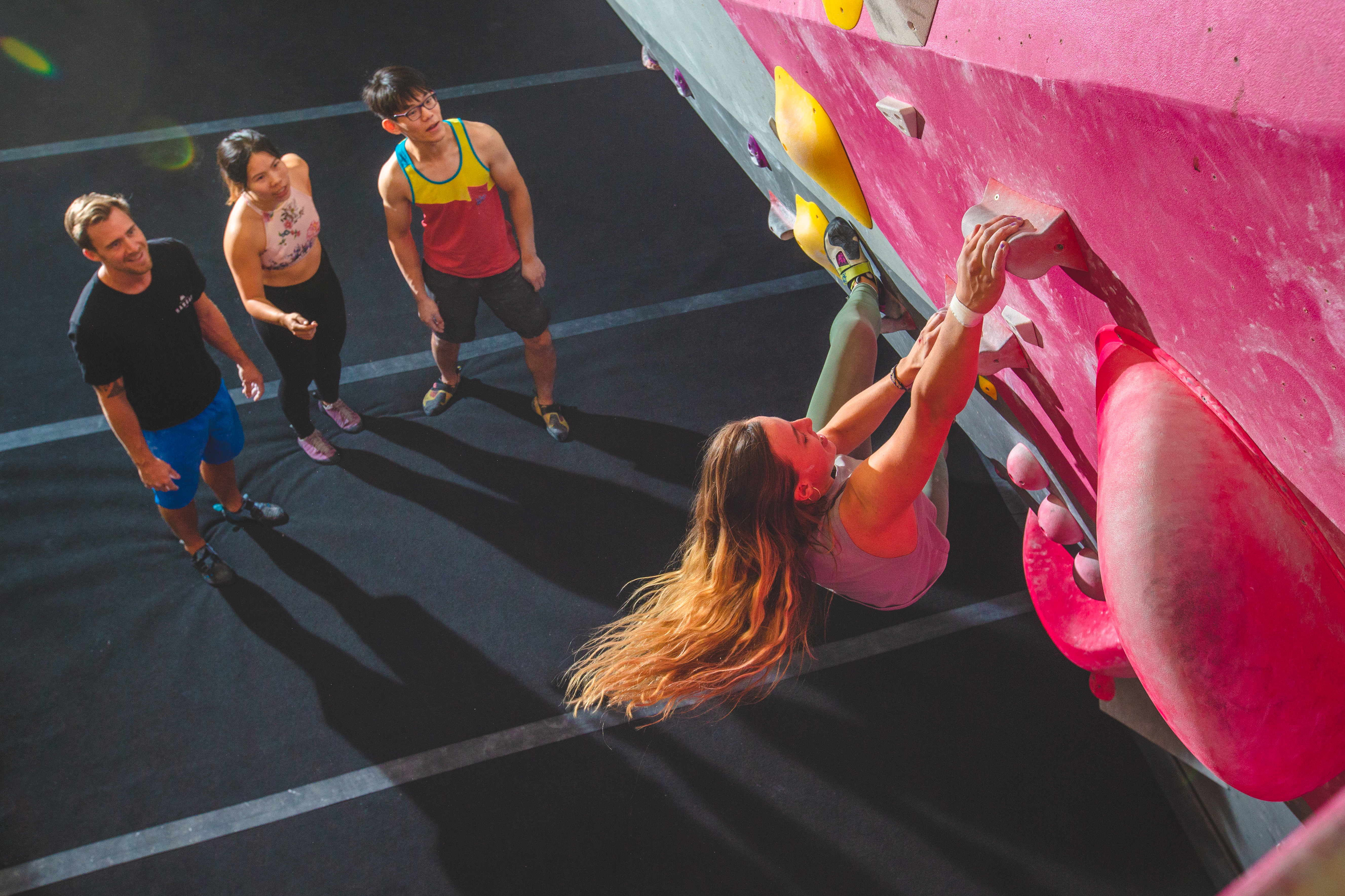 A woman on a climbing wall, with a group of friends watching below