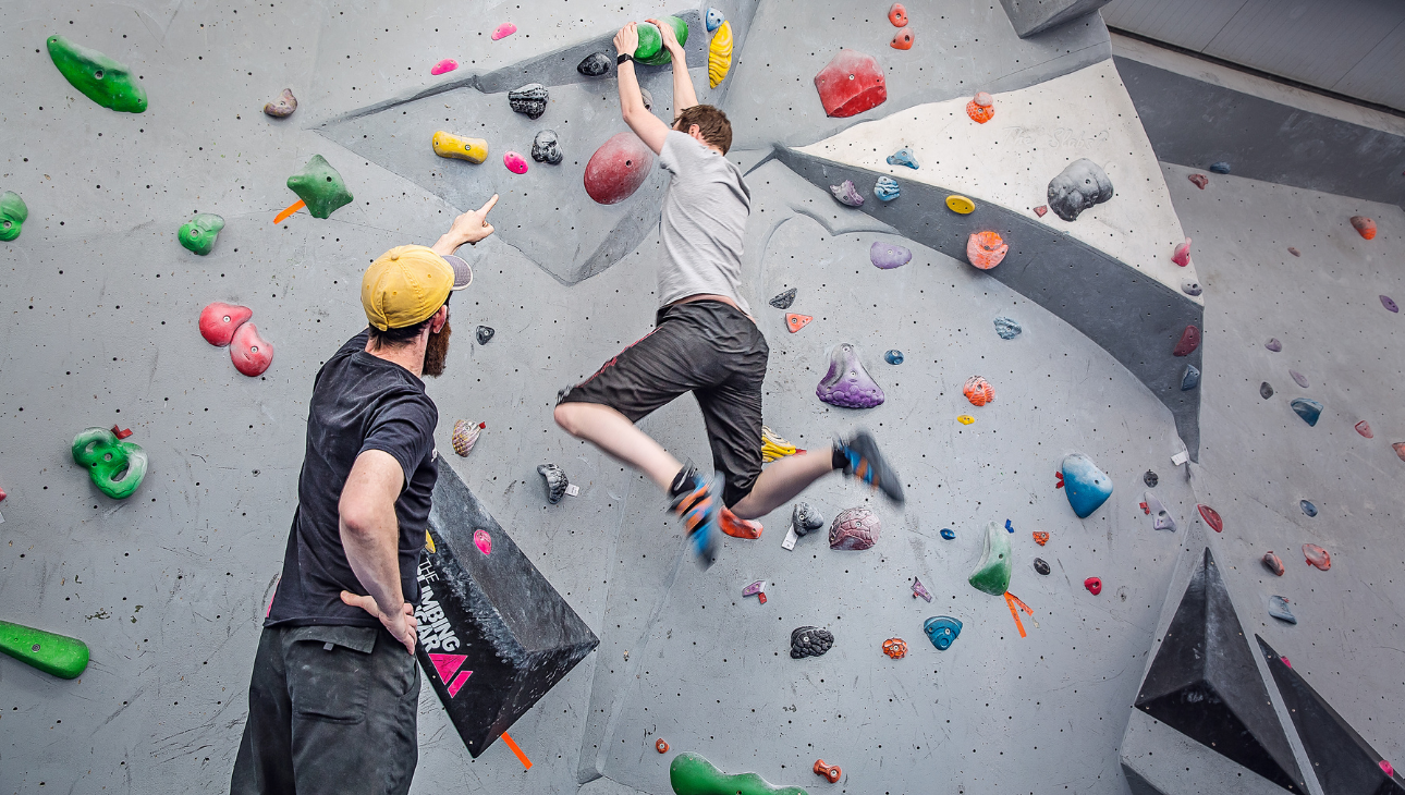 A man pointing out some beta for another man on the climbing wall at The Climbing Hangar