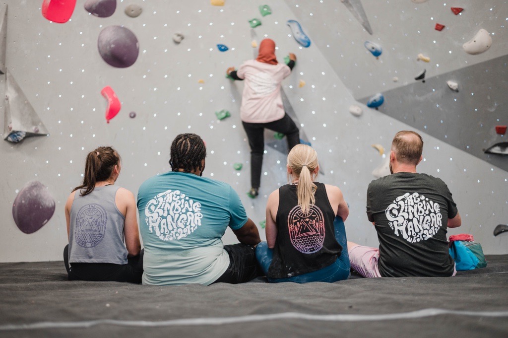 A group of people sat on the mats at a climbing wall